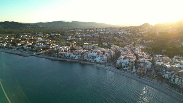 Aerial drone perspective of costal city Javea - Xabia. Sunset point. Sun going down behind the mountains. Panoramic view of all region. Drone panning right. Travel destination in Spain, Costa Blanca
