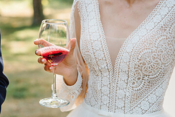 The bride is holding a glass of red wine outdoors. The girl has a beautiful dress and neckline...