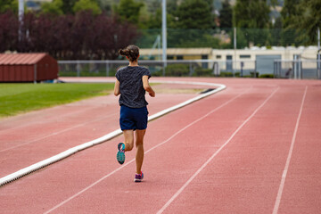 Back view of a young woman running on a stadium track; back view of a young athlete jogging on a running track