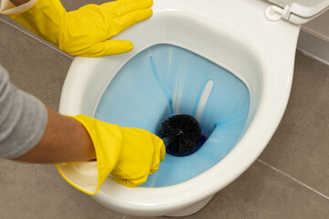 Close up of hands wearing yellow protective rubber gloves to deep clean a white, modern, ceramic...