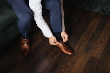 Brown leather shoe lacing. Businessman in white shirt and suit trousers. Groom getting ready for the wedding. Wearing clothes background. Dressing up male fashion. Business fashion hotel room.	
