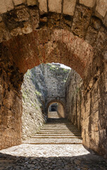 The sun casts warm tones on the brick archway and cobblestones, guiding through the mysterious tunnel Strada del Soccorso towards the Brescia castle historic heart