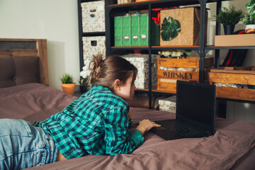 Beautiful young woman working on laptop while lying on bed at home.