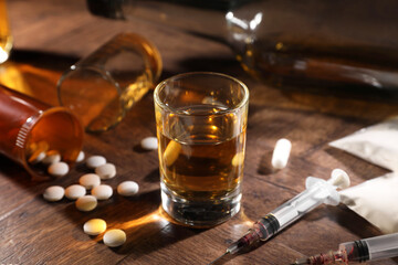 Alcohol and drug addiction. Whiskey in glass, syringes, pills and cocaine on wooden table