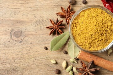 Curry powder in bowl and other spices on wooden table, flat lay. Space for text