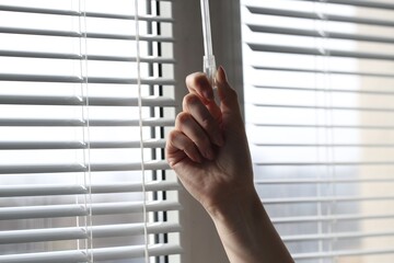 Woman opening white blinds at home, closeup