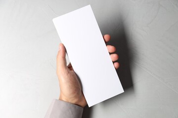 Man holding white blank card at light grey table, top view. Mockup for design