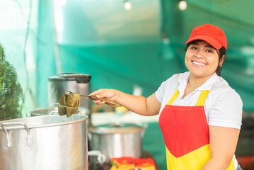 Latin woman fair cook smiling at camera, showing tamale from pot. 
