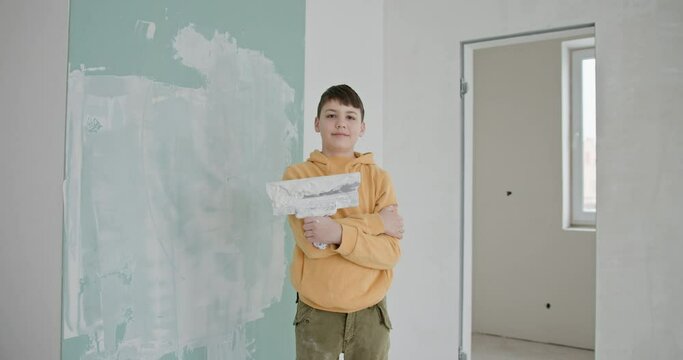 A young boy wearing a yellow hoodie and holding a paint roller stands proudly in a room with freshly painted walls. Self-repair, and the joy of making home improvements together.