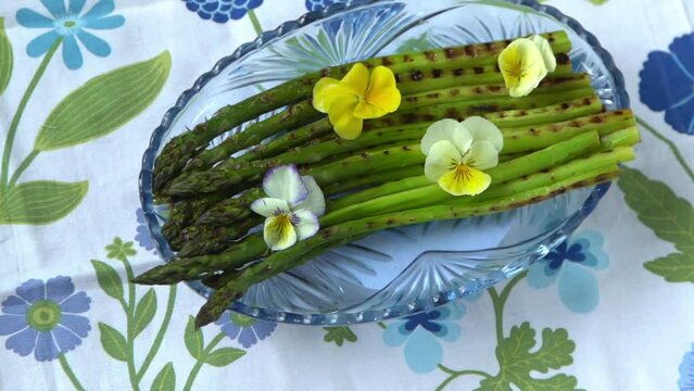 Green asparagus food. Spring vegetable on blue plate. Pansy flowers. Asparagus grill cooking eat. Floral tablecloth on the table top view