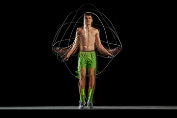 Fotobehang Gymnastiek Full-length of muscular, athletic young man in motion, training, jumping rope against black background with stroboscope effect. Concept of sport, active and healthy lifestyle, endurance and strength  © master1305