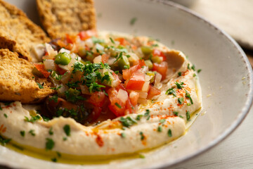 Traditional chickpea hummus with cut pepper and onion in the center served with toast. - obrazy, fototapety, plakaty