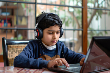 An enthusiastic Indian boy, sporting wireless headphones, focuses on a learning webinar and online lecture on his laptop.