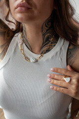 Young woman with a tattoo shows off jewelry on her neck and arm - a necklace with freshwater pearls and a ring