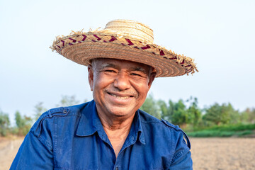 Happily smiling elderly farmer man in straw hat standing on agricultural area and looking at the camera, portrait, close-up