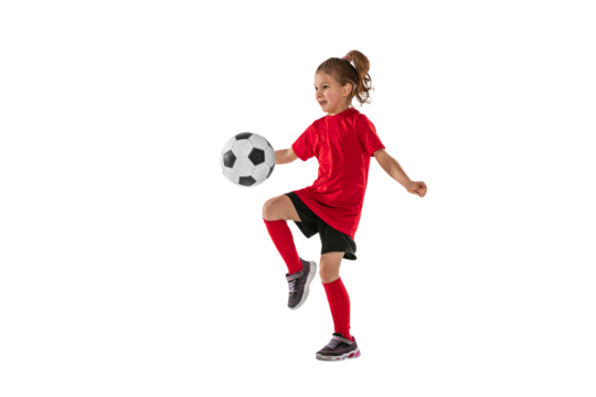 Portrait of girl, child, football player in red uniform training, kicking ball with knee against transparent background. Sportive and active kid. Concept of action, team sport game, energy, vitality.