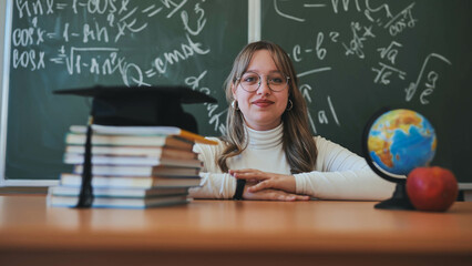 A schoolgirl wearing glasses poses against a background of books, an apple, a globe and a graduation cap.