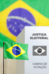 Bandeira brasileira decorando local de votação com a cabine de votação da Justiça Eleitoral do Brasil. Urna eletrônica e eleições no Brasil.