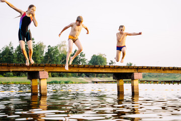 Teen girl in swimsuit and two smaller boys jumping from a bridge into a lake at sunset. Happy...