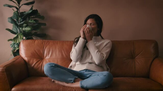 Beautiful attractive woman sitting on sofa , flirting , posing and looking into and away from camera. Fashion concept. Drinking coffee, cosy jumper