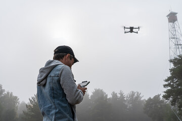 man controls a remote control of a UAV against the sky and a high old tower for monitoring forests....
