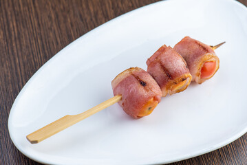 Three pieces of bacon wrapped tomato on a skewer.