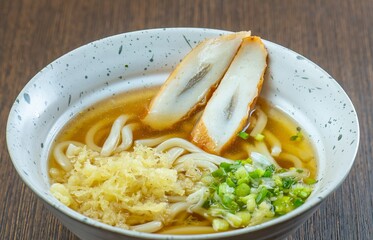 A bowl of udon noodles with a clear broth, topped with tempura and green onions.