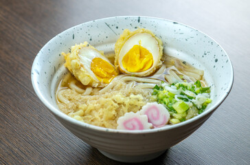 A bowl of udon noodles with a soft-boiled egg and tempura.