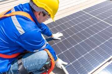 A solar panel installer wearing a hard hat and safety gear is installing solar panels on a roof.