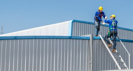 Two construction workers wearing safety gear climb up a ladder to the roof of a building