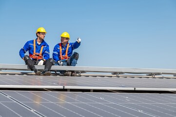 Two engineers in hard hats and safety gear inspecting solar panels on a rooftop