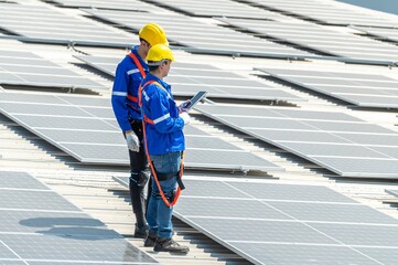 Two solar panel workers wearing safety gear are inspecting a large solar panel array on a...