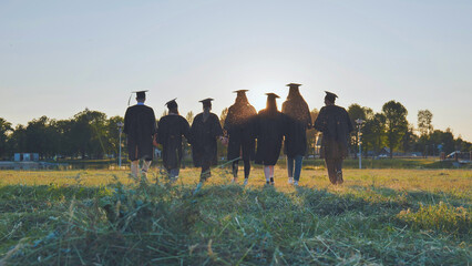 College graduates walk at sunset holding hands.
