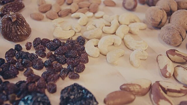 Raisins, dried fruits, almonds, figs, brazil nuts, walnuts, cashew nuts, cashews, dried cranberries on a wooden table. Close up. Interior, kitchen. Studio lighting. High quality 4k footage