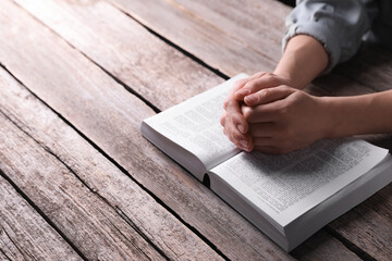 Religion. Christian woman praying over Bible at wooden table, closeup. Space for text
