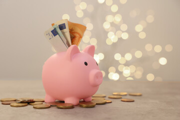 Pink piggy bank, euro banknotes and coins on grey table against blurred lights, space for text