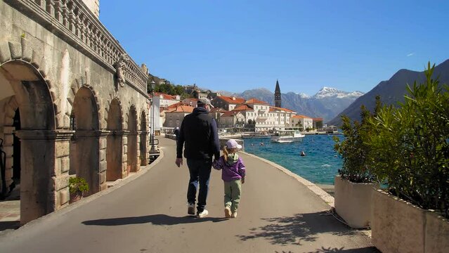 A father and daughter walking hand in hand through the old town along the coast. Perast, Montenegro.