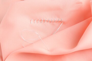Sewing needle with thread and stitches on coral cloth, top view