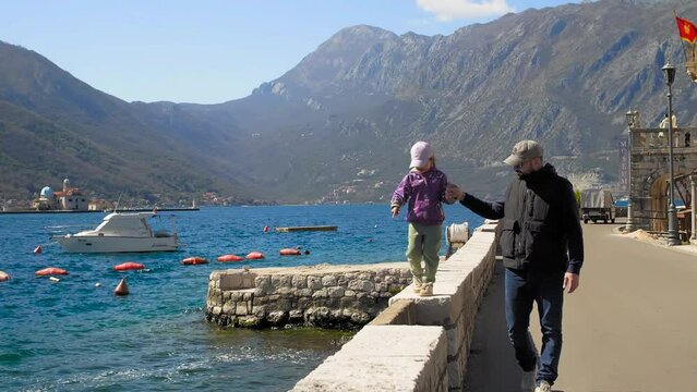 A father and daughter walking hand in hand through the old town along the coast. Perast, Montenegro. Front view.