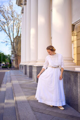 elegant middle age woman in white vintage dress near theater with antique colonnades