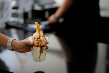 Hand holding glass of ice latte coffee with ice cream and on black table at coffee shop.