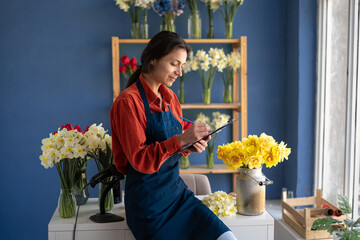 Florist small business owner checking her fresh flowers stock and writing in clipboard, managing a flowers shop. Small business