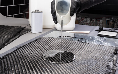 hand pouring epoxy resin on woven carbon fiber reinforcement cloth. Production manufacturing of ...