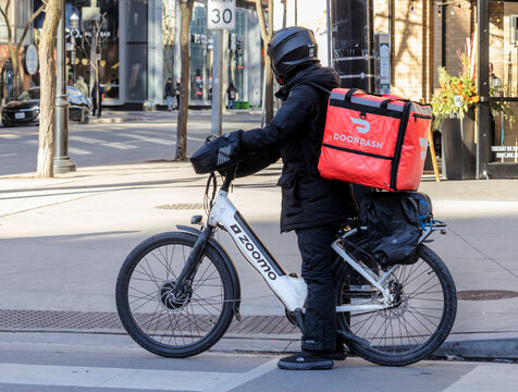 Toronto, Canada, January 4, 2024; A DoorDash food delivery courier on an electric bicycle, or e-bike, with the distinctive red back pack on a downtown street