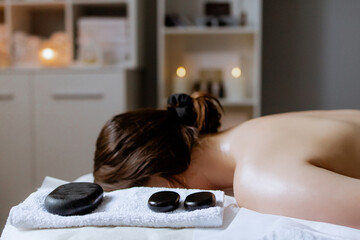 Woman enjoying hot stone massage at spa salon. Professional masseur making stone therapy. Relaxing...