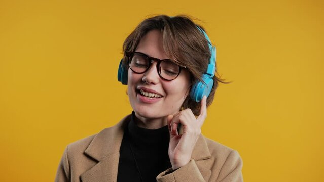 Happy business woman listening music, enjoying headphones, yellow background