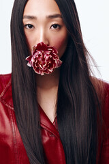 Beautiful woman with long black hair wearing red jacket and holding flower in mouth, outdoor...