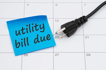 Utility bill due with electric cord plug and sticky note on a calendar