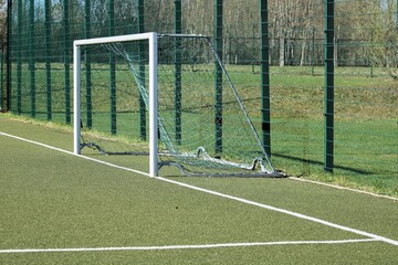 an artificial turf soccer field with a soccer goal on it and a green fence behind it