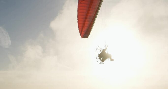 Powered Paragliding PPG, pilot wears a back-pack motor and flies in front of sunset sky and ocean water, slow motion. Extreme air sport action in Portugal at summer vacation. Low paramotor flying man.